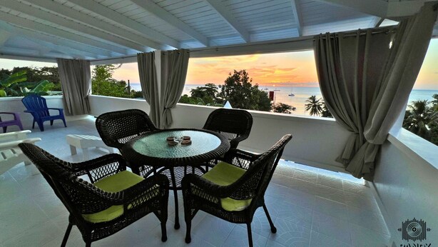 Un balcone con un tavolo rotondo e sedie in vimini, con vista sul tramonto.