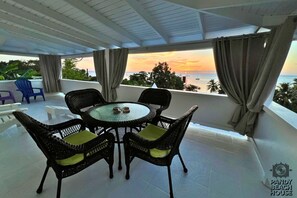 A balcony with a round table and wicker chairs, overlooking a sunset view. - Ocean View 3-bedroom Apartment in Grand Anse with AC (Saint George)