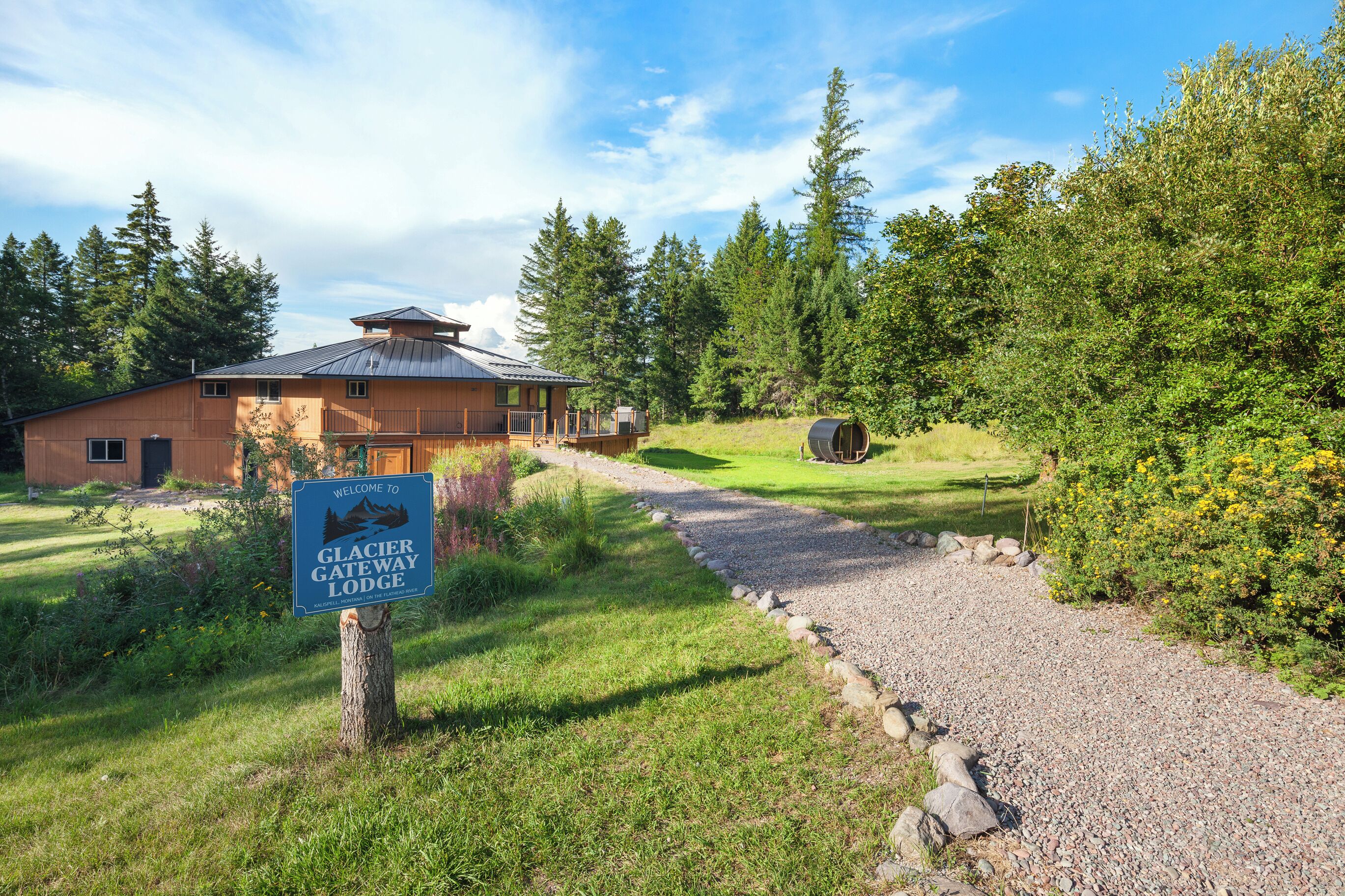 A lodge entrance with a sign, a gravel path, and surrounding greenery.