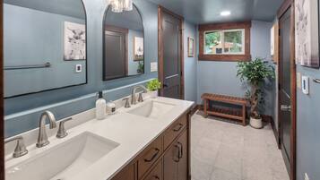 A bathroom with a double sink, wooden cabinets, a bench, and a potted plant.