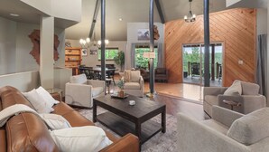 A spacious living area with a high ceiling, a central coffee table, leather sofas, and a wooden accent wall.