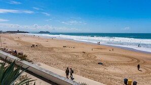 Une plage animée, un navire à l’horizon et un ciel dégagé.