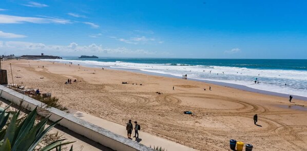 A beach with people, a ship in the distance, and a clear sky.