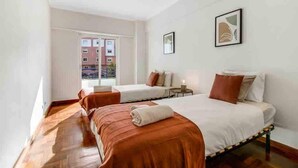 Une chambre d’hôtel avec deux lits, une petite table et une fenêtre donnant sur des immeubles.