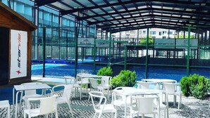 Un espace extérieur abrité, doté de tables et de chaises, une piscine et une vue sur les bâtiments en arrière-plan.