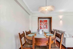 A dining area with a round table, wooden chairs, a hanging light fixture, and a framed artwork on the wall.