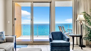 A room with a view of the ocean, a sliding glass door, a blue armchair, a small table, and a lamp.