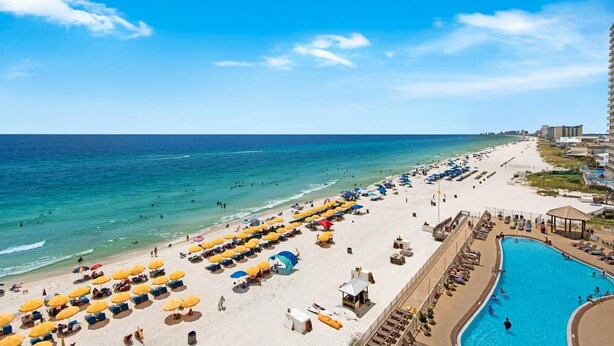 A beach resort with a pool, sun loungers, and umbrellas.