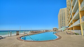 A swimming pool with a tiled deck, a beach view, and a high-rise building with balconies.