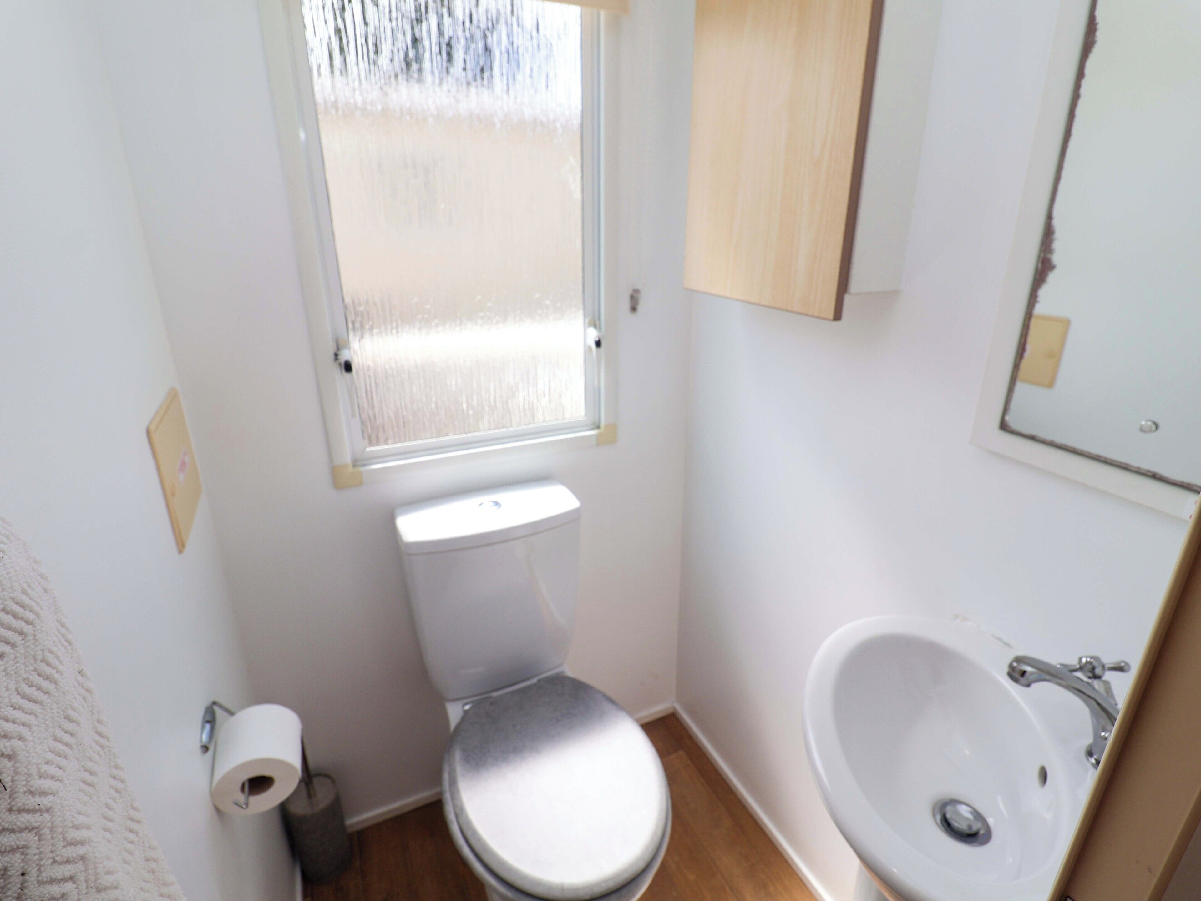 A small, compact bathroom with a toilet, sink, and a window above the toilet.