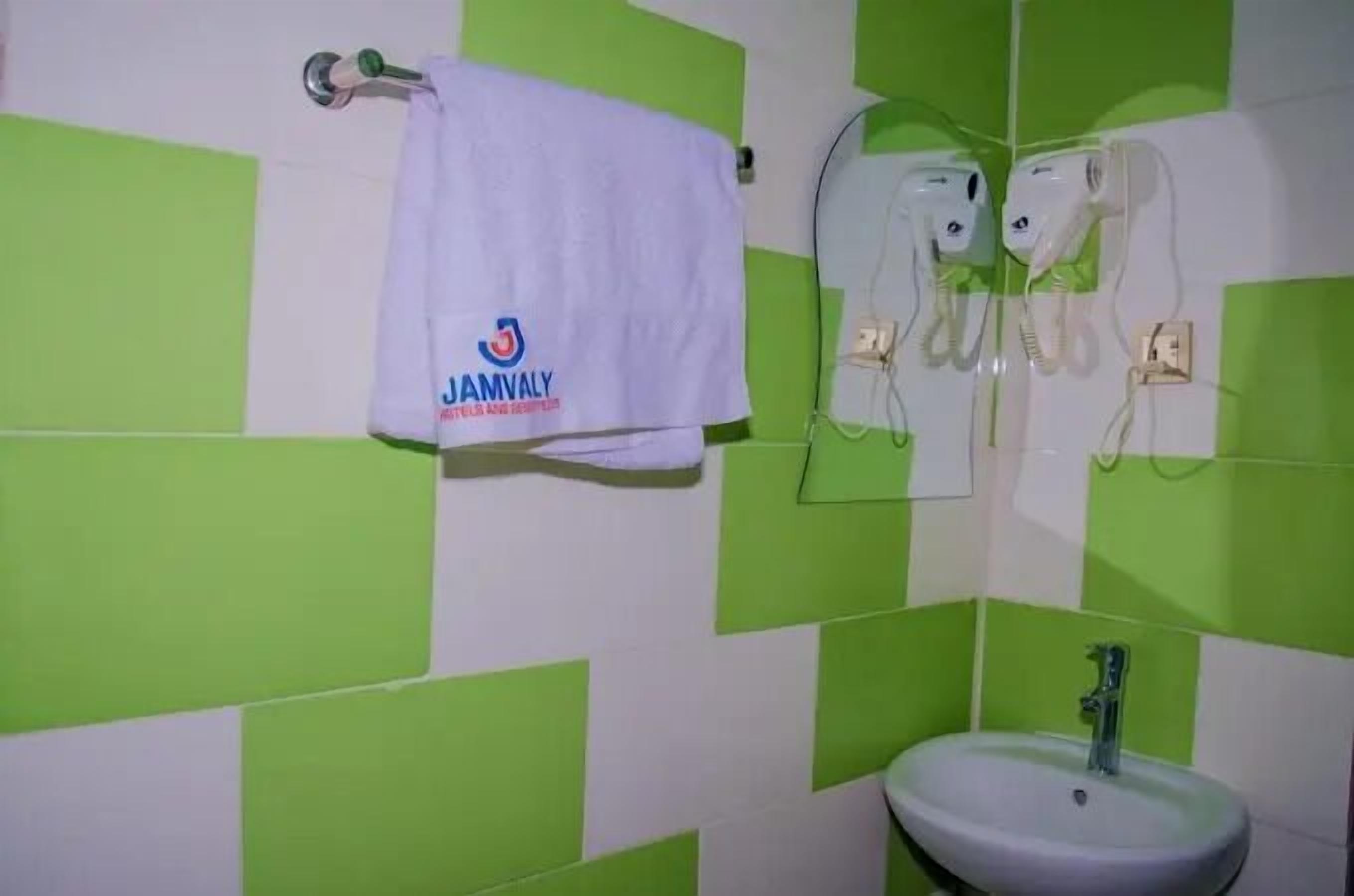 A bathroom with green and white checkered tiles, a white towel with "JAMVALY" logo, and a sink with a mirror above it.