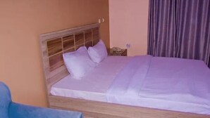 Una cama individual con cabecera de madera, una silla azul y una mesita de noche con lámpara.