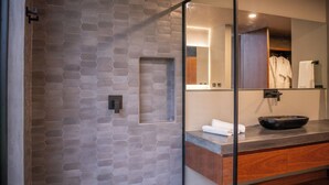 A modern bathroom with a hexagonal tile wall, a wooden vanity, a black bowl, and a mirror reflecting a robe and towel. - Casa Audaz: Private Pool, Jacuzzi & Daily Cleaning in a Peaceful Escape (Circasia)