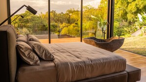 A modern bedroom with a large window, a bed, a floor lamp, and a wooden side table. - Casa Audaz: Private Pool, Jacuzzi & Daily Cleaning in a Peaceful Escape (Circasia)
