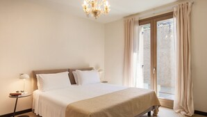 A bedroom with a large bed, a chandelier, a bedside table with a lamp, and a window with curtains. - Apartment Righini with Pool (Torri del Benaco)