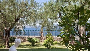 A garden with a statue, a stone wall, and a view of the sea. - Apartment Righini with Pool (Torri del Benaco)