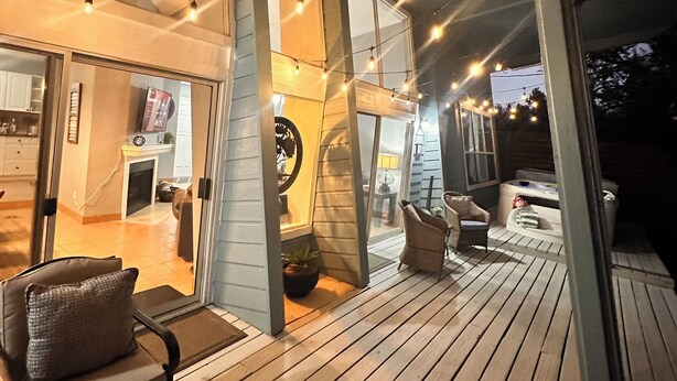 A wooden deck with outdoor seating, a glass door entrance, and string lights.