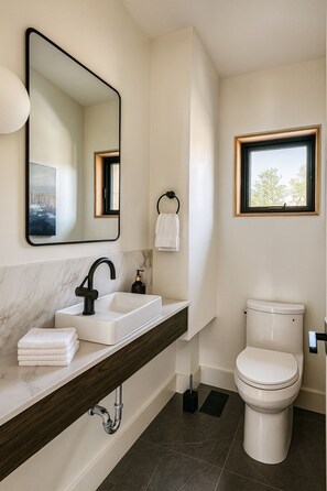 Un baño moderno con lavamanos de mármol, grifo negro y retrete.