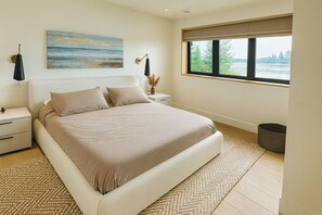 Un dormitorio moderno con una cama grande, una mesita de noche, una lámpara de noche, una ventana con vistas al exterior y un cuadro en la pared.