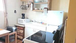 A compact kitchen with a microwave, stove, sink, and hanging pots. There is a wooden table and chairs, and a refrigerator.