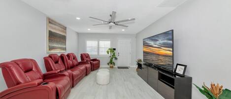 A modern living room with a red leather sofa, a flat-screen TV, and a ceiling fan.