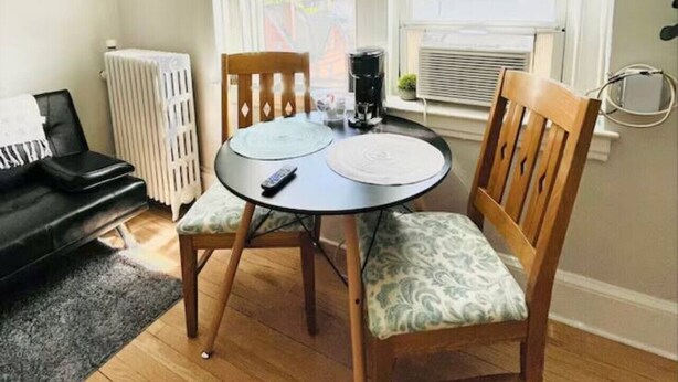 A small dining area with a round table, two chairs, a black coffee maker, and a radiator. - Modern Studio Retreat (New Haven)