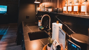 Una cuina moderna amb detalls de fusta, un rentaplat i una màquina de cafè, i una zona de bar amb ampolles.