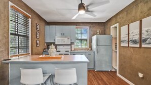 A kitchen with a central island, bar stools, a microwave, and a refrigerator. - Chic Boho Treehouse Studio in Morningside (Miami)