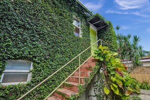 A house with a staircase covered in green ivy, a small window, and a wooden fence in the background. - Chic Boho Treehouse Studio in Morningside (Miami)