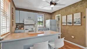 A kitchen with white cabinets, a central island, and a ceiling fan. - Chic Boho Treehouse Studio in Morningside (Miami)