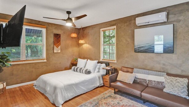A bedroom with a bed, a sofa, a ceiling fan, and a large window. - Chic Boho Treehouse Studio in Morningside (Miami)