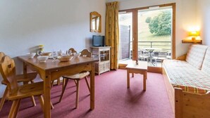 Una habitación acogedora con una mesa de madera para comer, sillas, un sofá, un televisor y un balcón con vistas a zonas verdes.