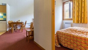 Una habitación pequeña y acogedora con una cama, un escritorio y sillas, y una ventana con cortinas.
