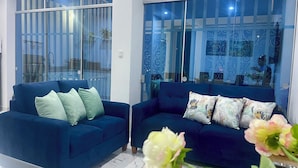 Una sala de estar moderna con dos sofás azules, un separador de vidrio y vistas al exterior.