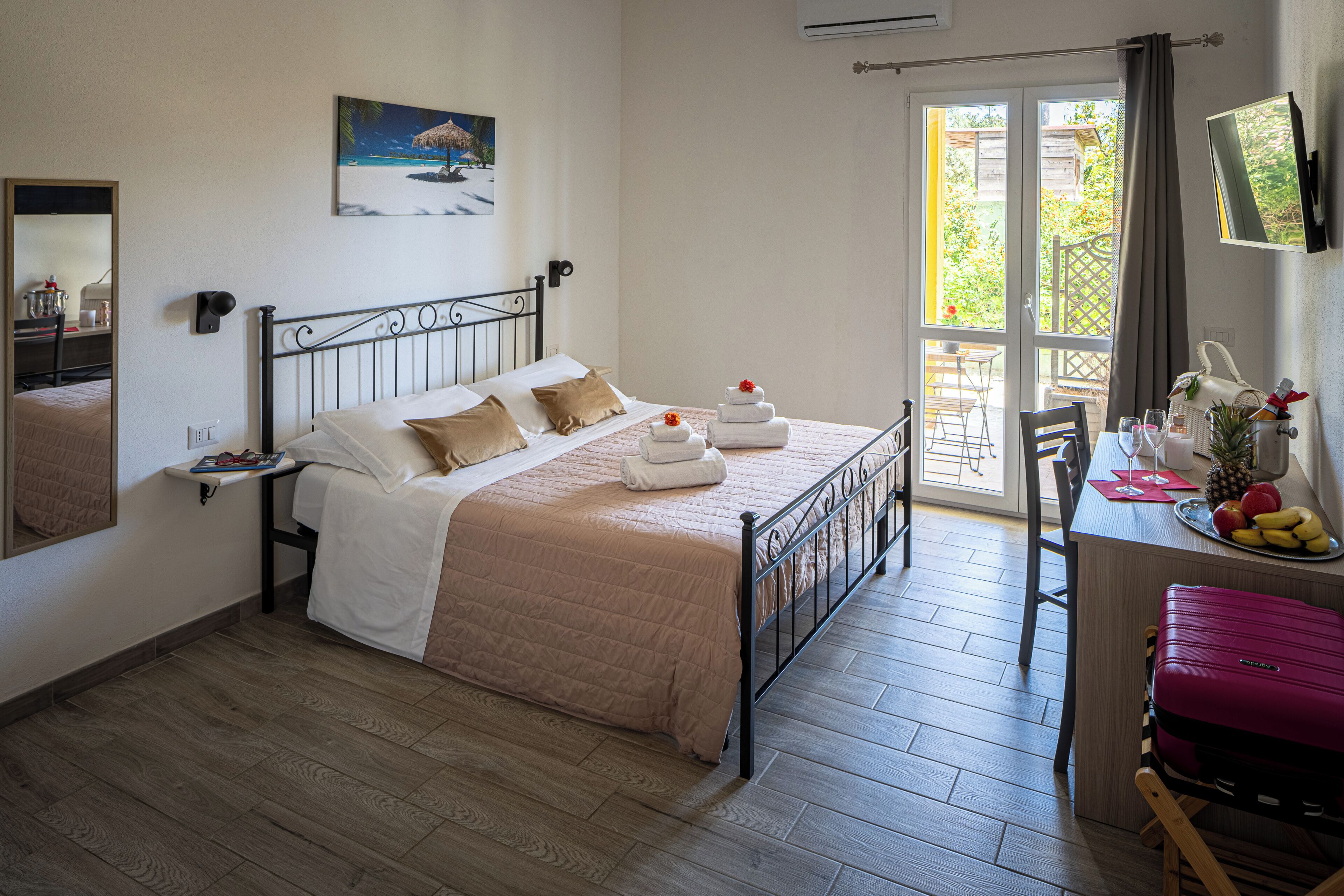 Une chambre d’hôtel avec un lit, un bureau et une chaise, une valise, un téléviseur et une fenêtre donnant sur un paysage verdoyant.