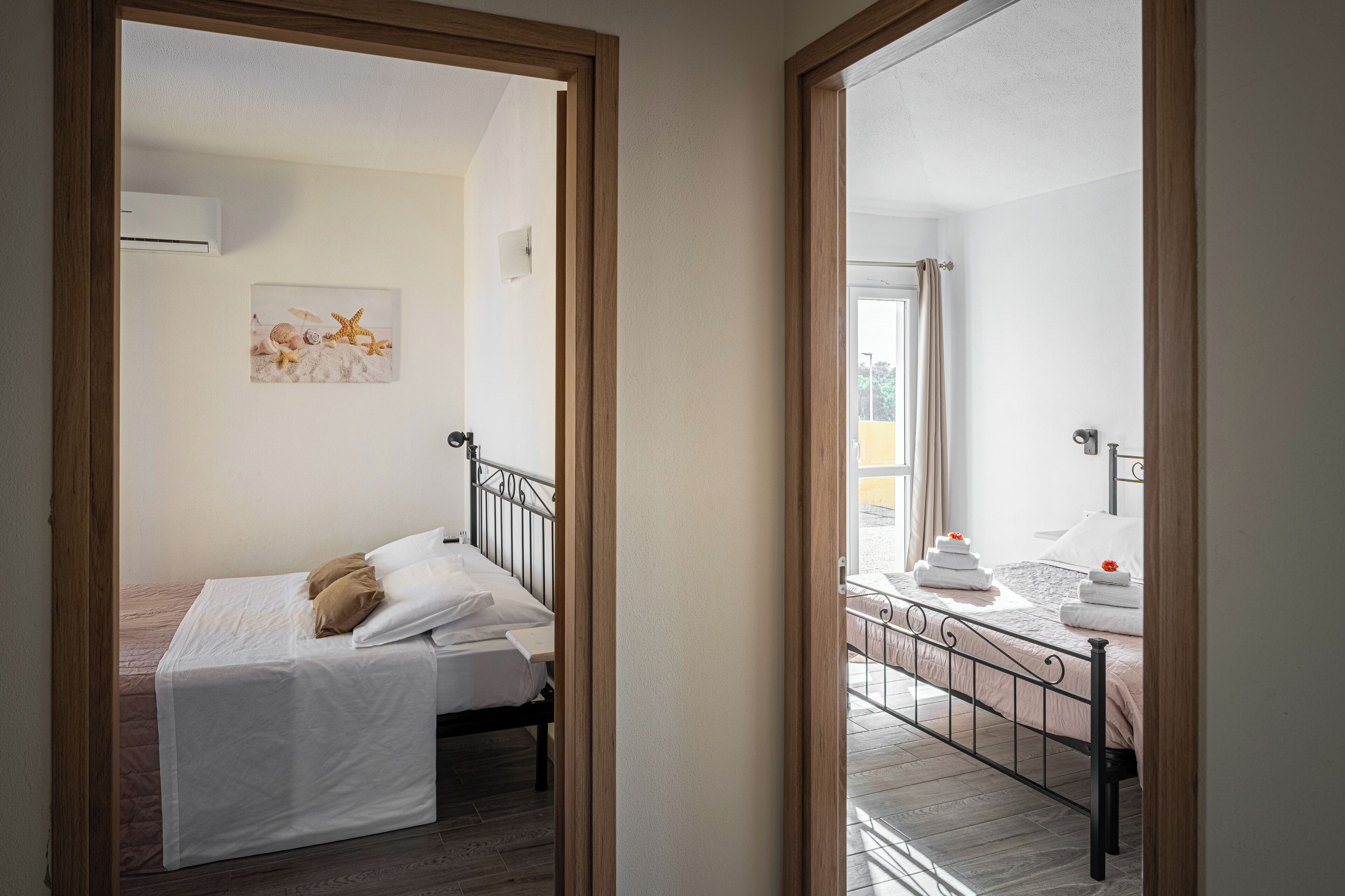 A bedroom with a bed, a small table with towels, a picture on the wall, and a window with curtains.