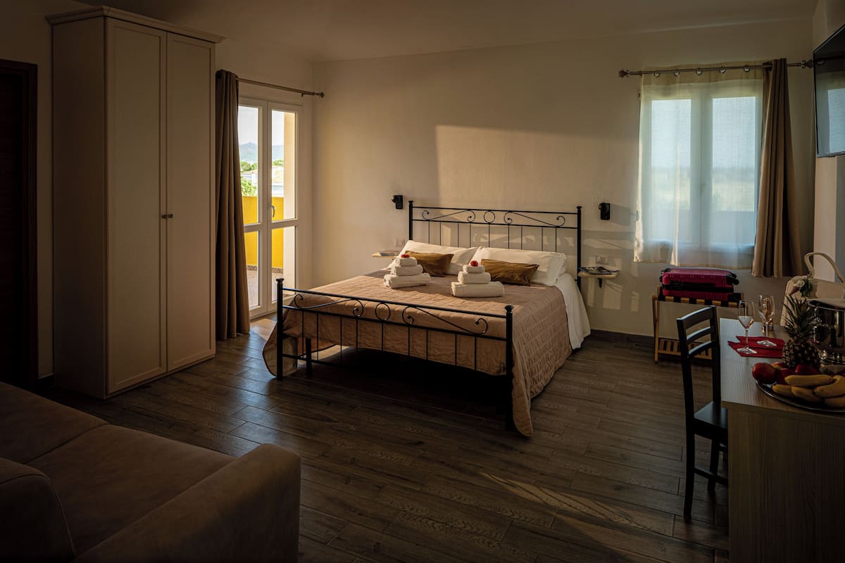 Un dormitorio con cama, armario, escritorio con silla y ventana con cortinas.
