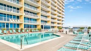 Ein Hotelpoolbereich mit mehreren Balkonebenen, einem Pool mit Metallleiter und Reihen von blauen und weißen Liegestühlen.