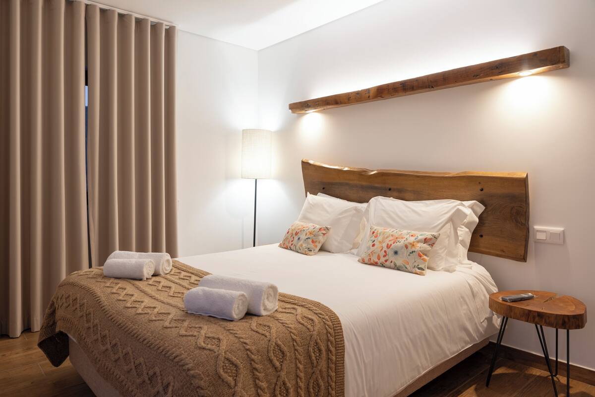 A neatly made bed with a wooden headboard, a bedside lamp, and a small wooden table.