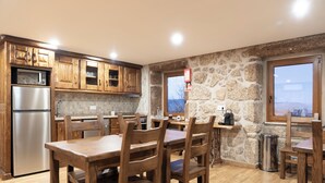 A kitchen with wooden cabinets, a stainless steel refrigerator, a dining table with chairs, and a stone wall. - Quinta do Limite Agroturismo (Covilhã)