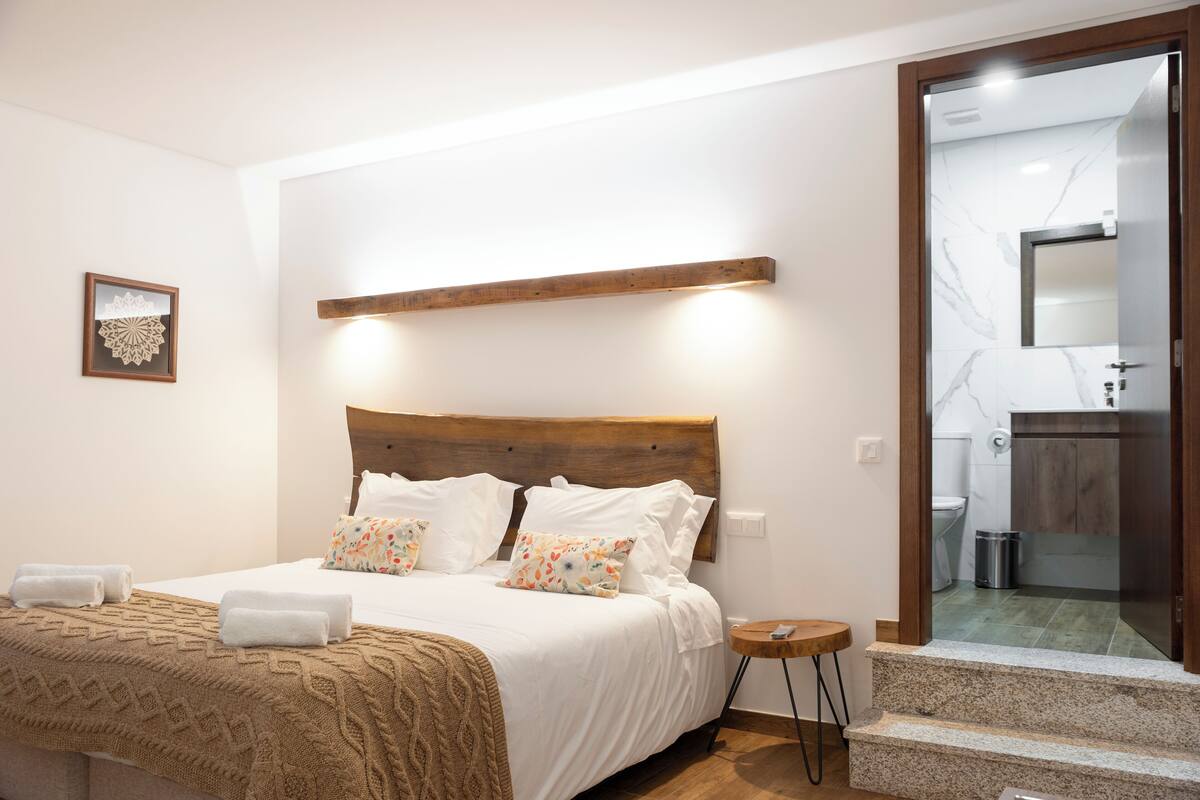 A neatly made bed with a wooden headboard, a small bedside table, and a framed picture on the wall.