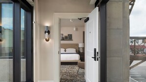 A hotel room with a bed, a nightstand, a lamp, and a view of the outside.