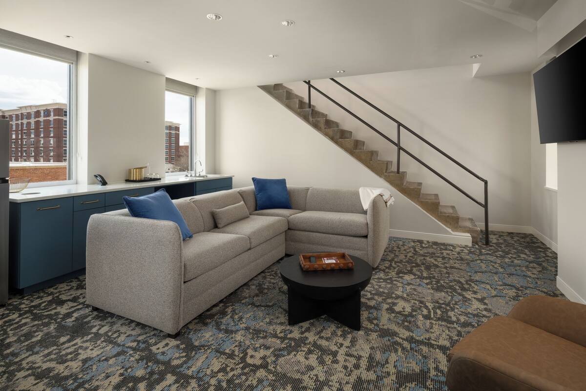 Una sala de estar moderna con un sofá modular, una mesa de centro, una escalera y vistas a la ciudad.