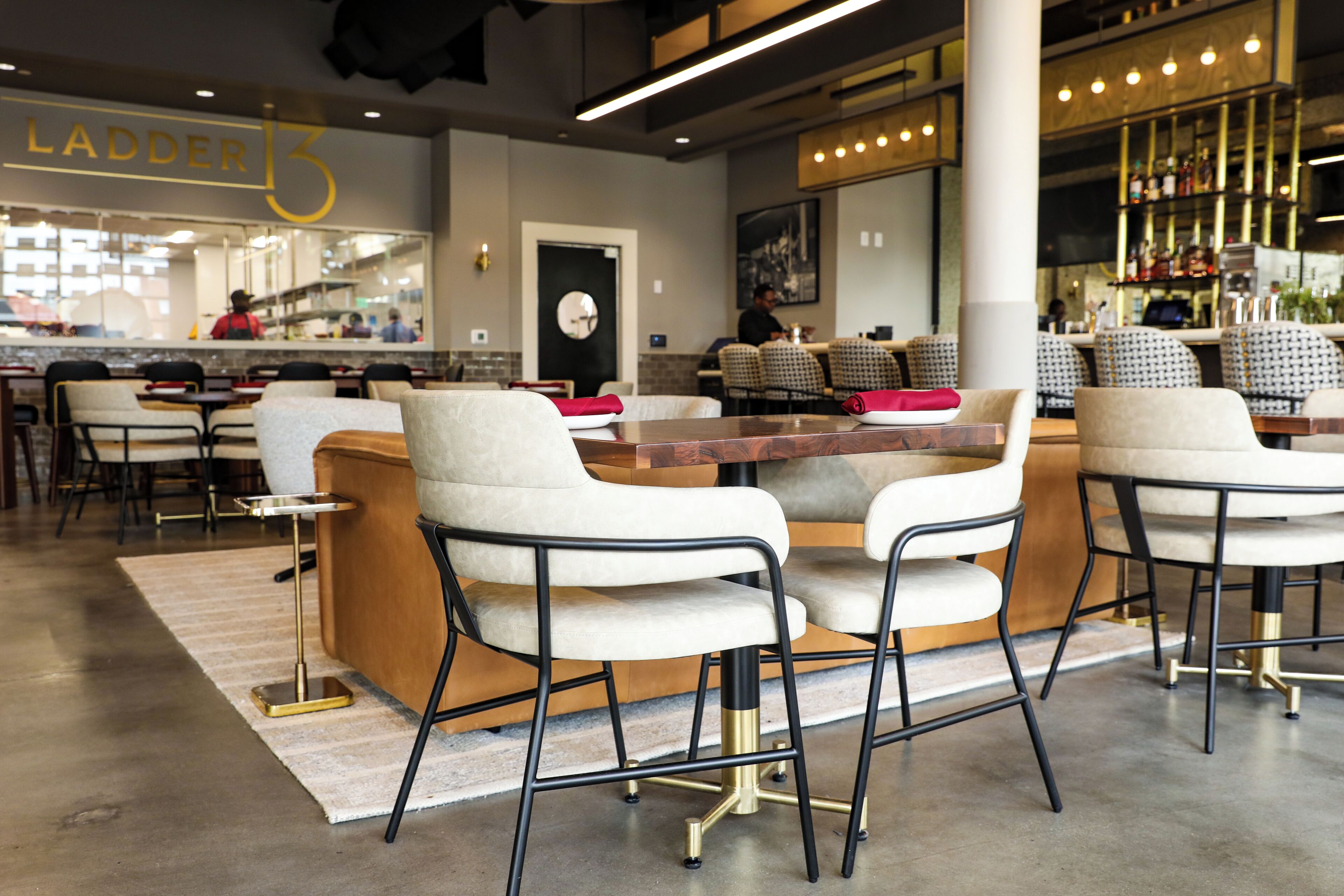 Eine moderne Bar mit Sitzgelegenheiten, einer Theke und einer sichtbaren Treppe mit der Aufschrift 'LADDER 13'.
