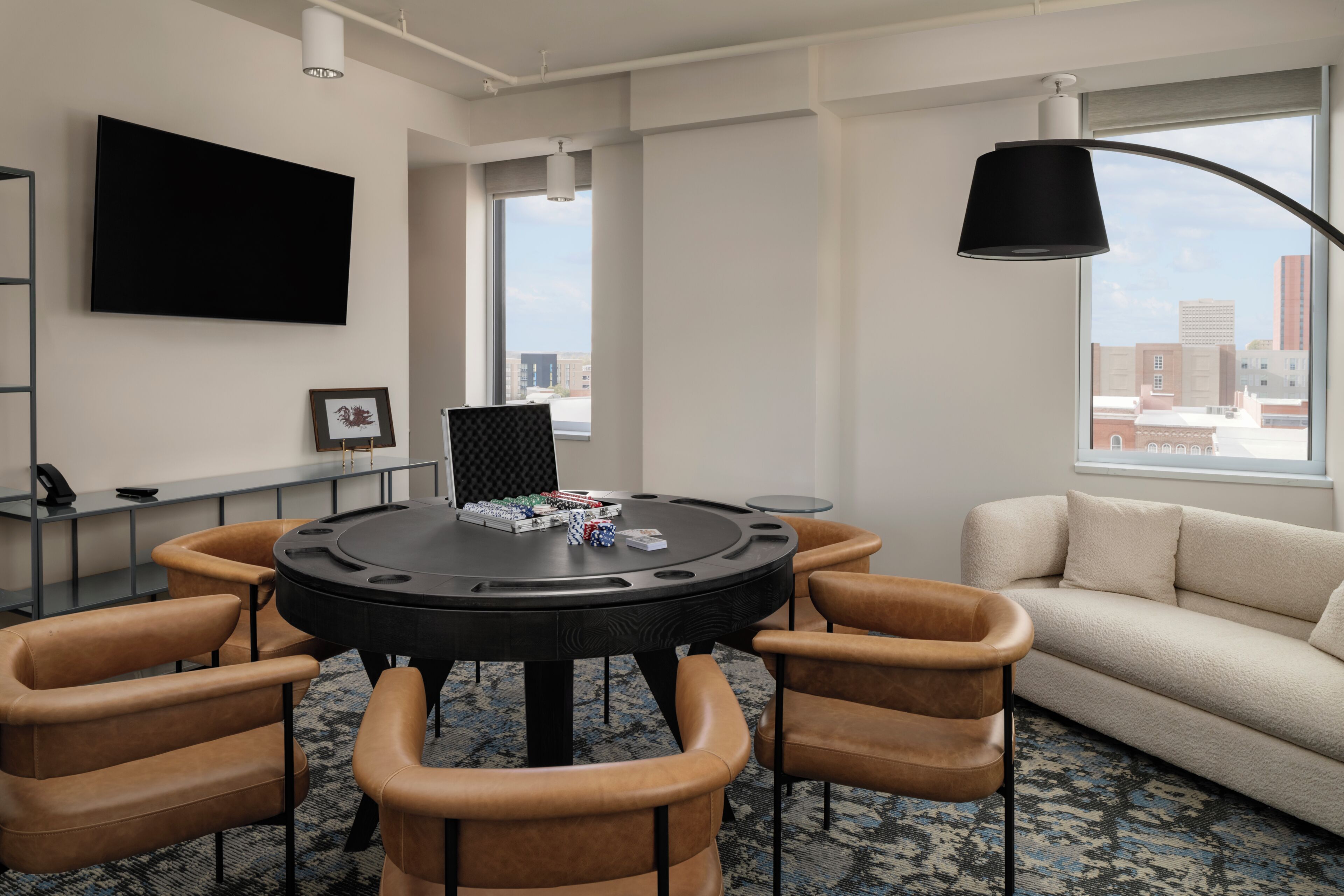 A modern room with a round table, leather chairs, a sofa, a flat-screen TV, and a city view.