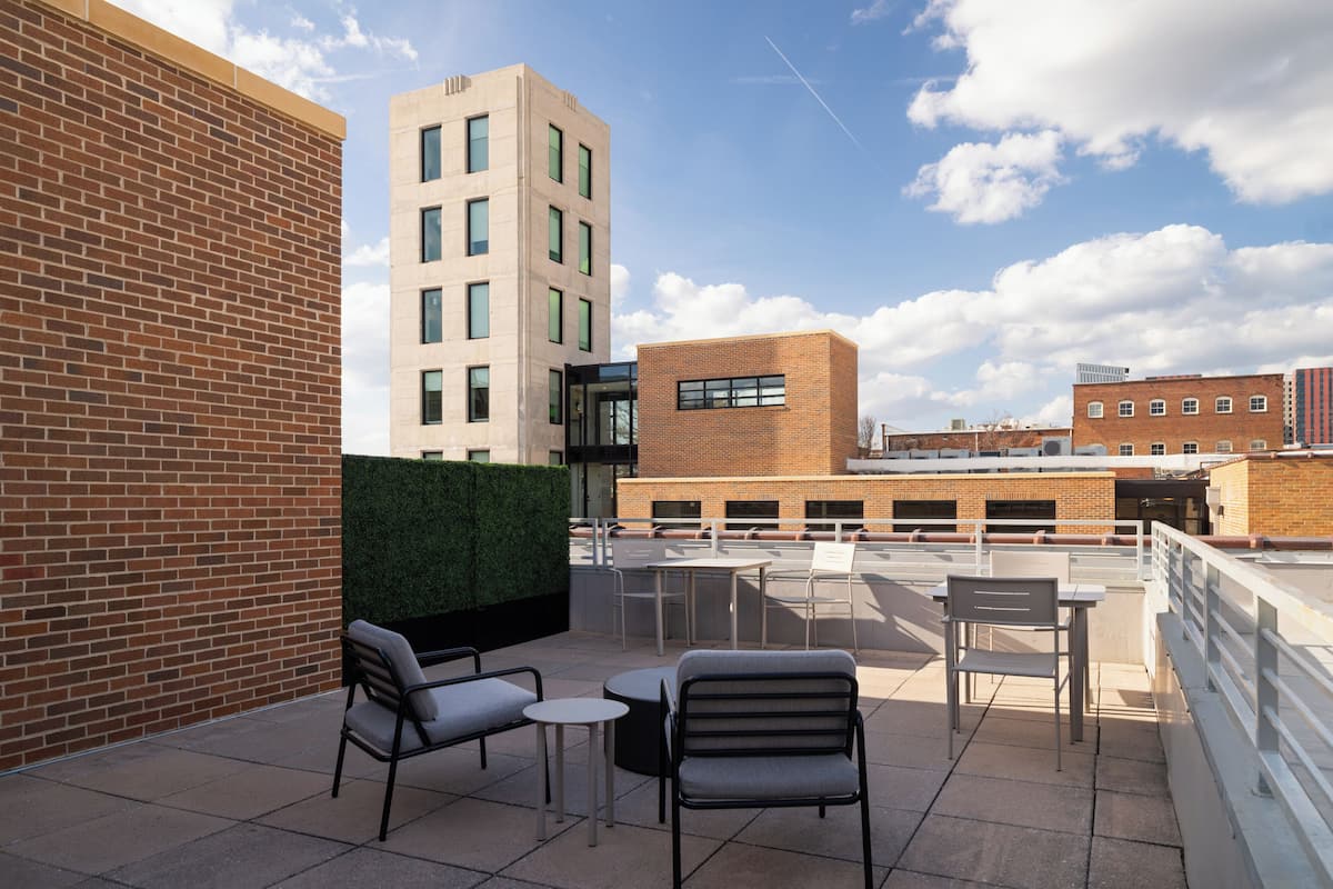 Una terraza en la azotea con mesas al aire libre, un muro de ladrillo y vistas de edificios circundantes.