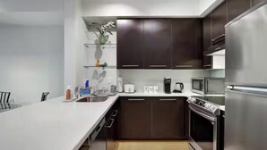 Une cuisine moderne avec des meubles de couleur sombre, des appareils en acier inoxydable et un plan de travail blanc.