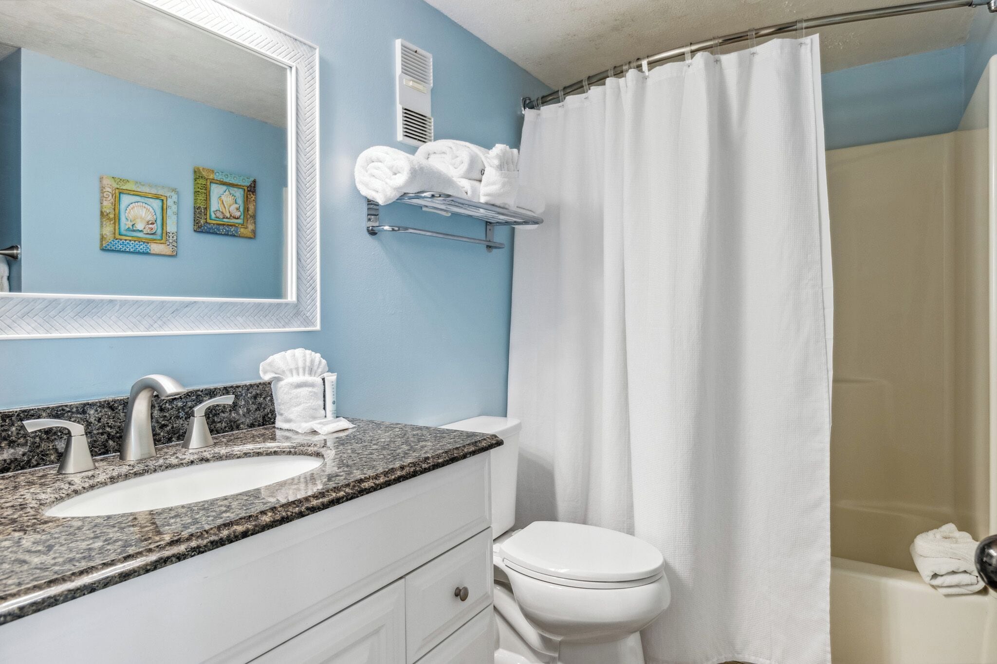 Un baño con pared azul, sanitarios blancos, encimera de granito y cortina de ducha.