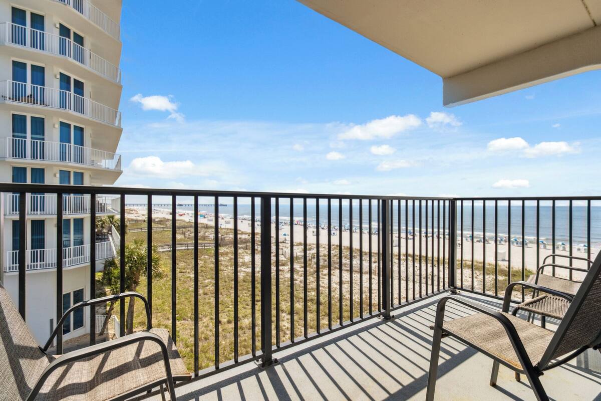 A balcony with two chairs, a view of the beach, and a building with multiple balconies.