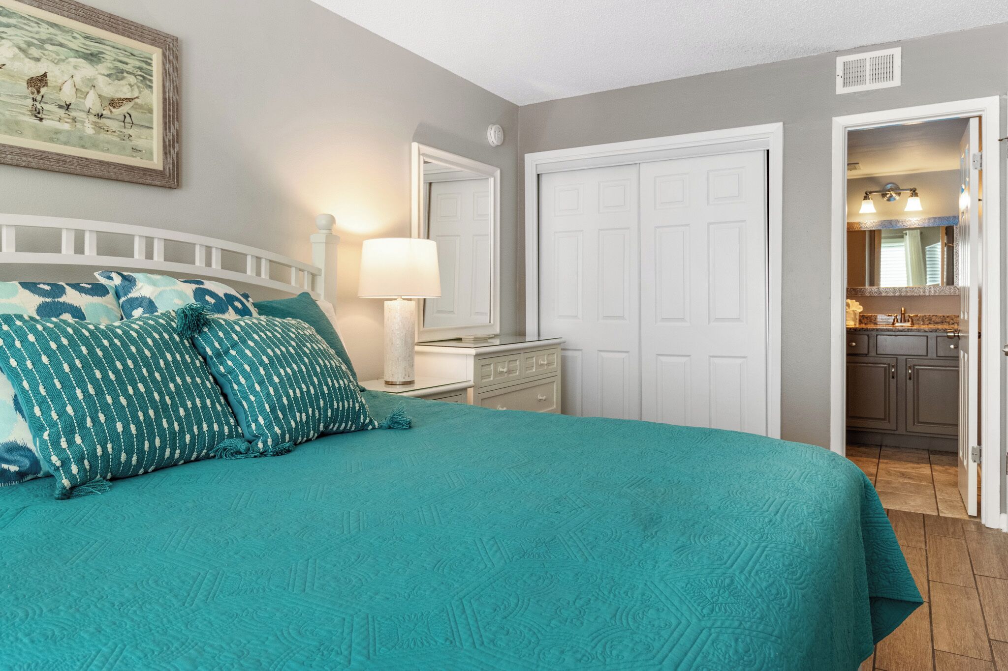 Une chambre à coucher avec un lit, une table de chevet, une commode et une salle de bain visible à travers une porte ouverte.
